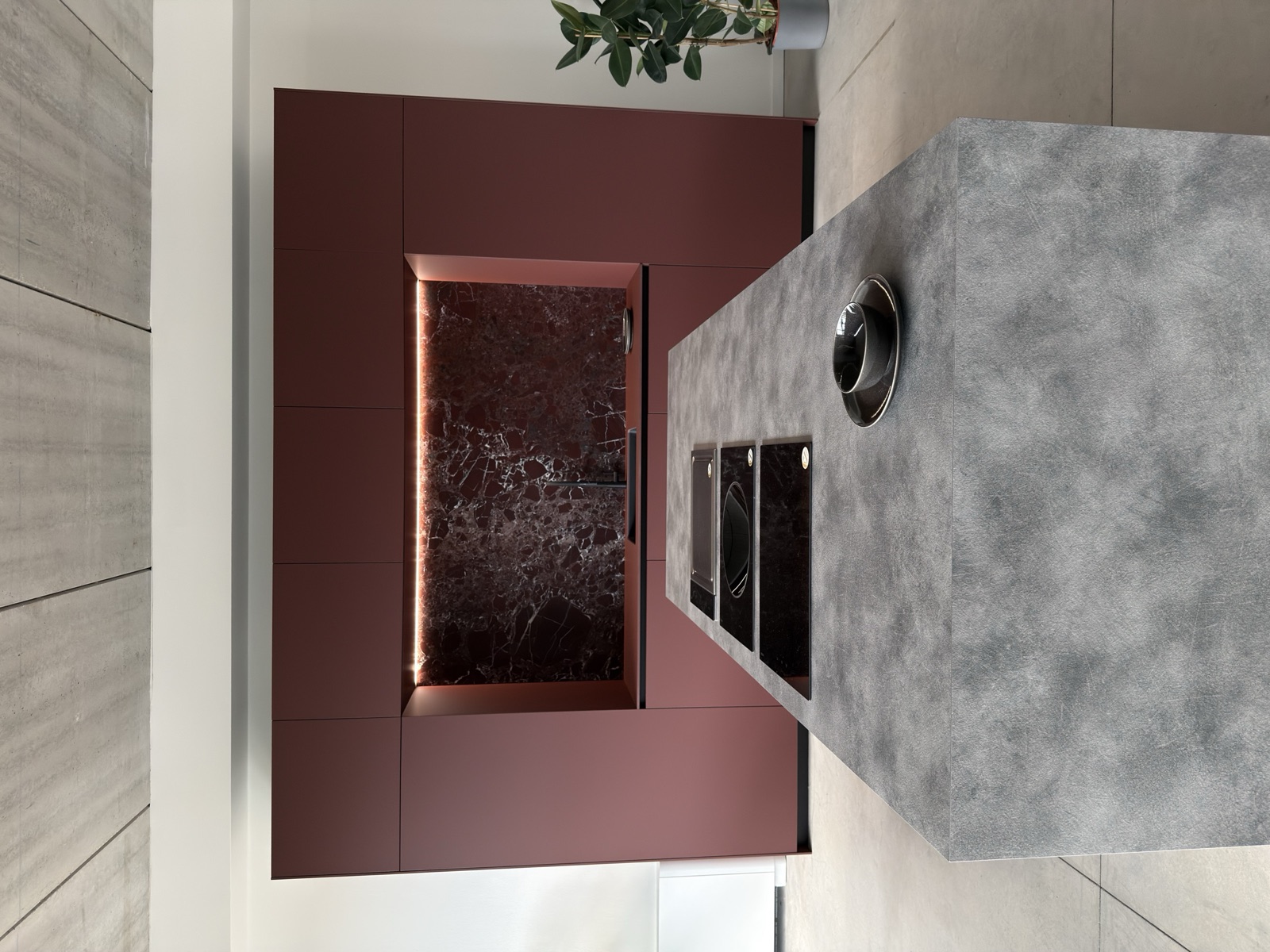 Showroom LA PI Cucine — cucina con isola in cemento materico e parete laccata bordeaux con backsplash in marmo Rosso Levanto